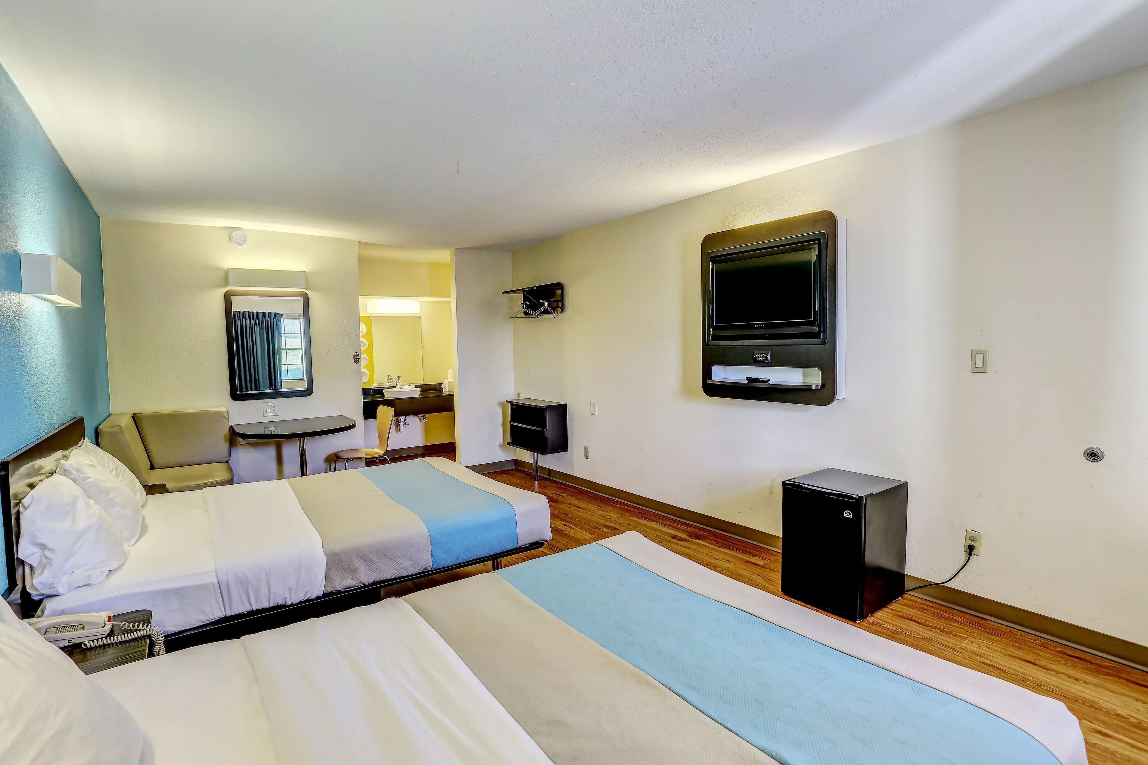 A hotel room with two beds, a desk, a chair, a TV, and a small black cabinet.