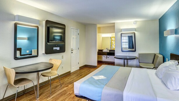 Una habitación de hotel con cama, escritorio, dos sillas, una mesita y un espejo.