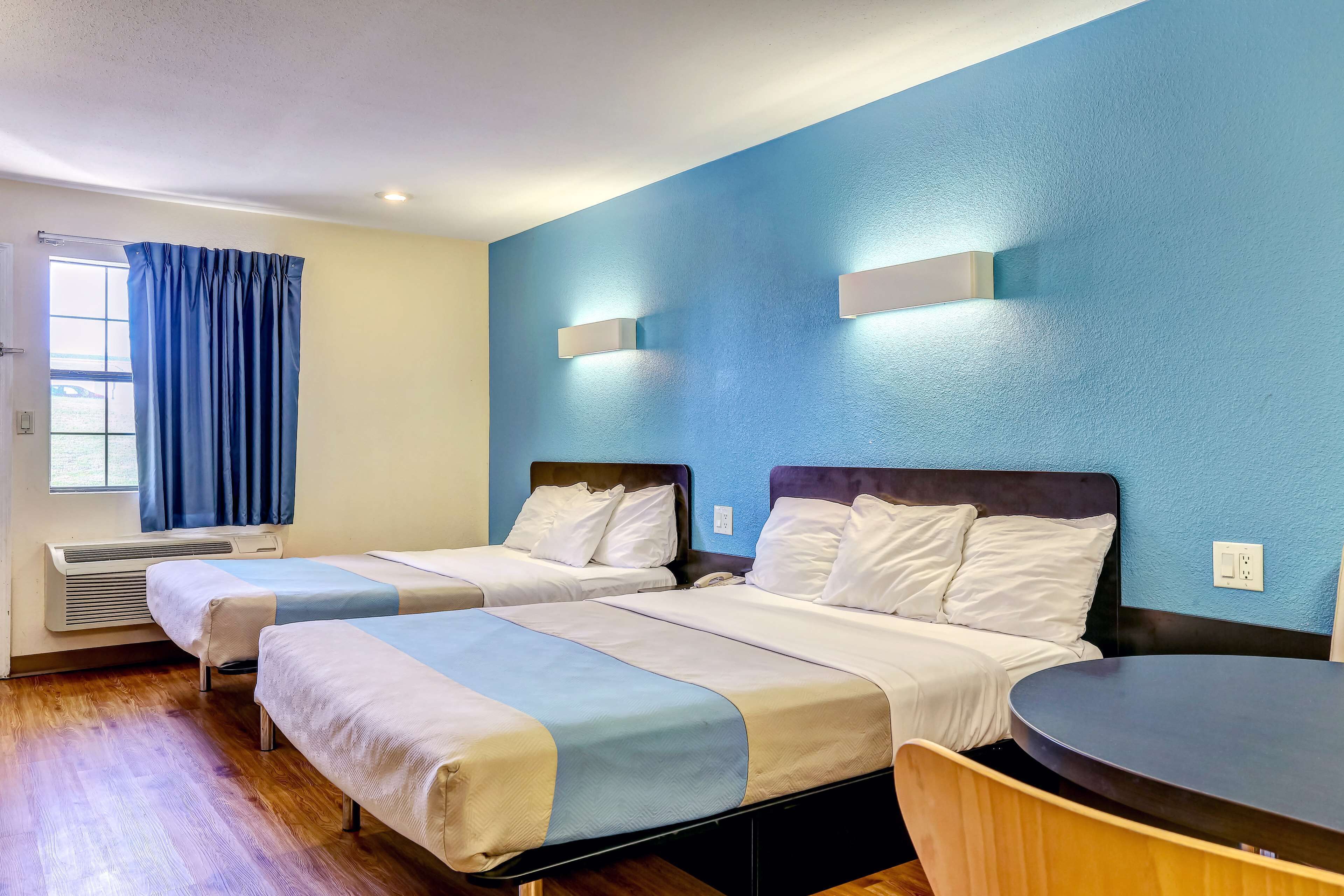 Una habitación de hotel con dos camas, una mesa redonda y una ventana con cortinas.