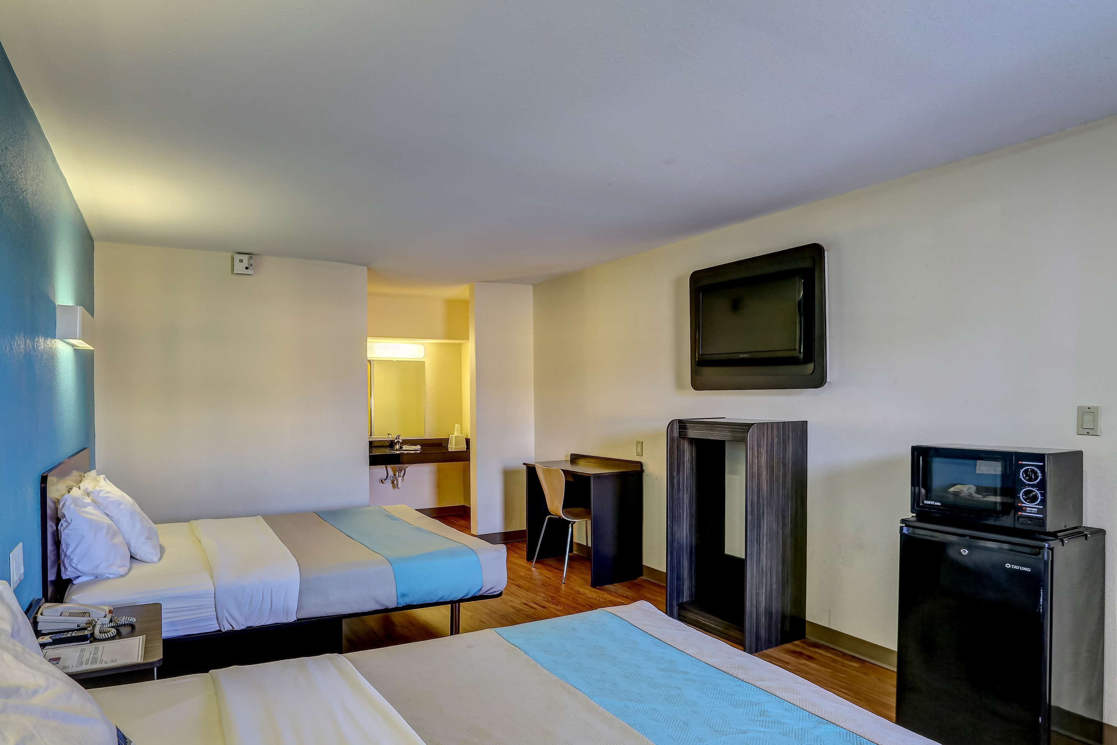 Habitación de hotel con dos camas, un escritorio, una silla, un televisor y un refrigerador.