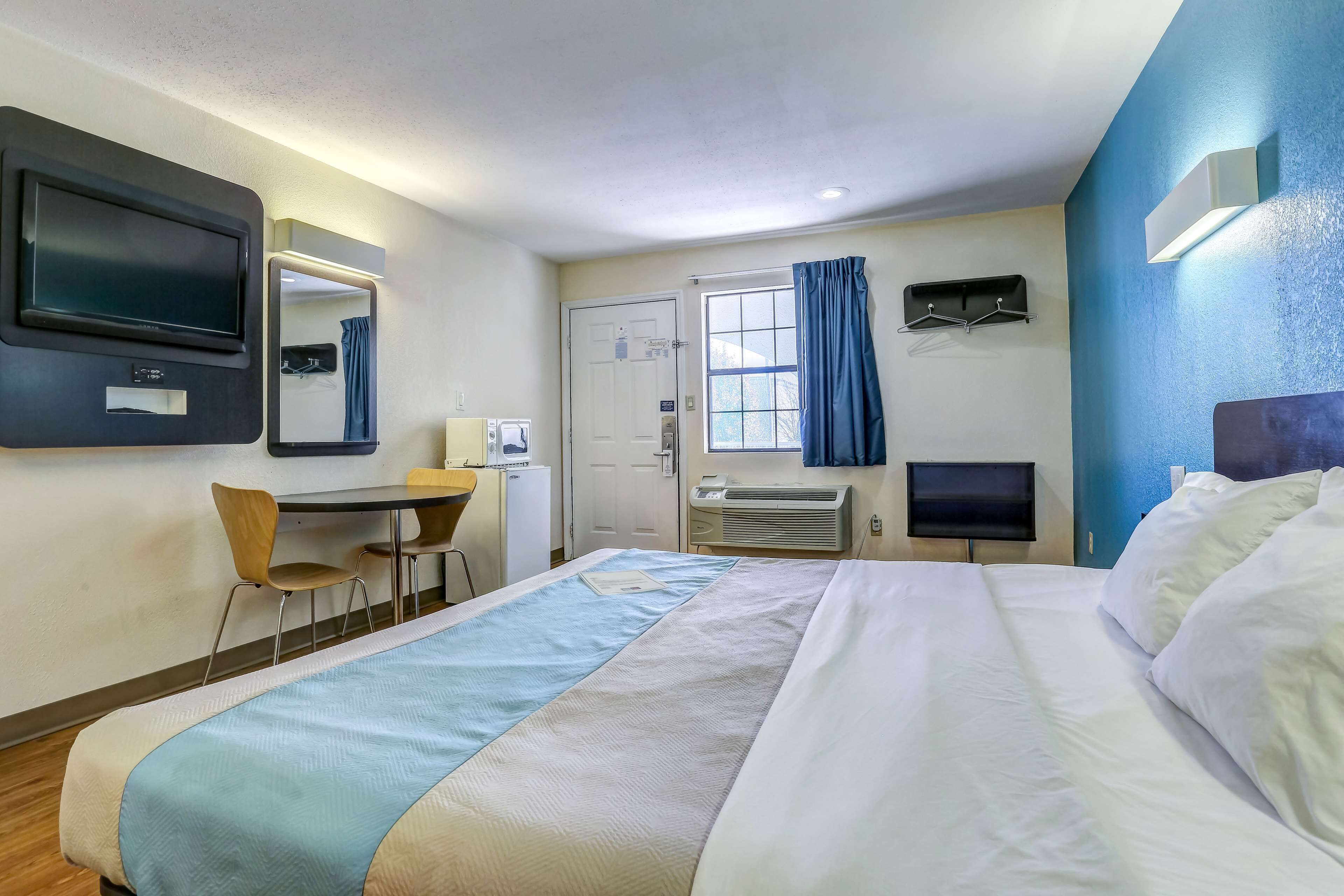 A hotel room with a bed, a desk, a chair, a television, and a window with curtains.