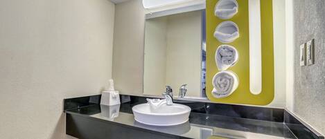 A modern bathroom with a black countertop, white sink, and a mirror with a green accent.