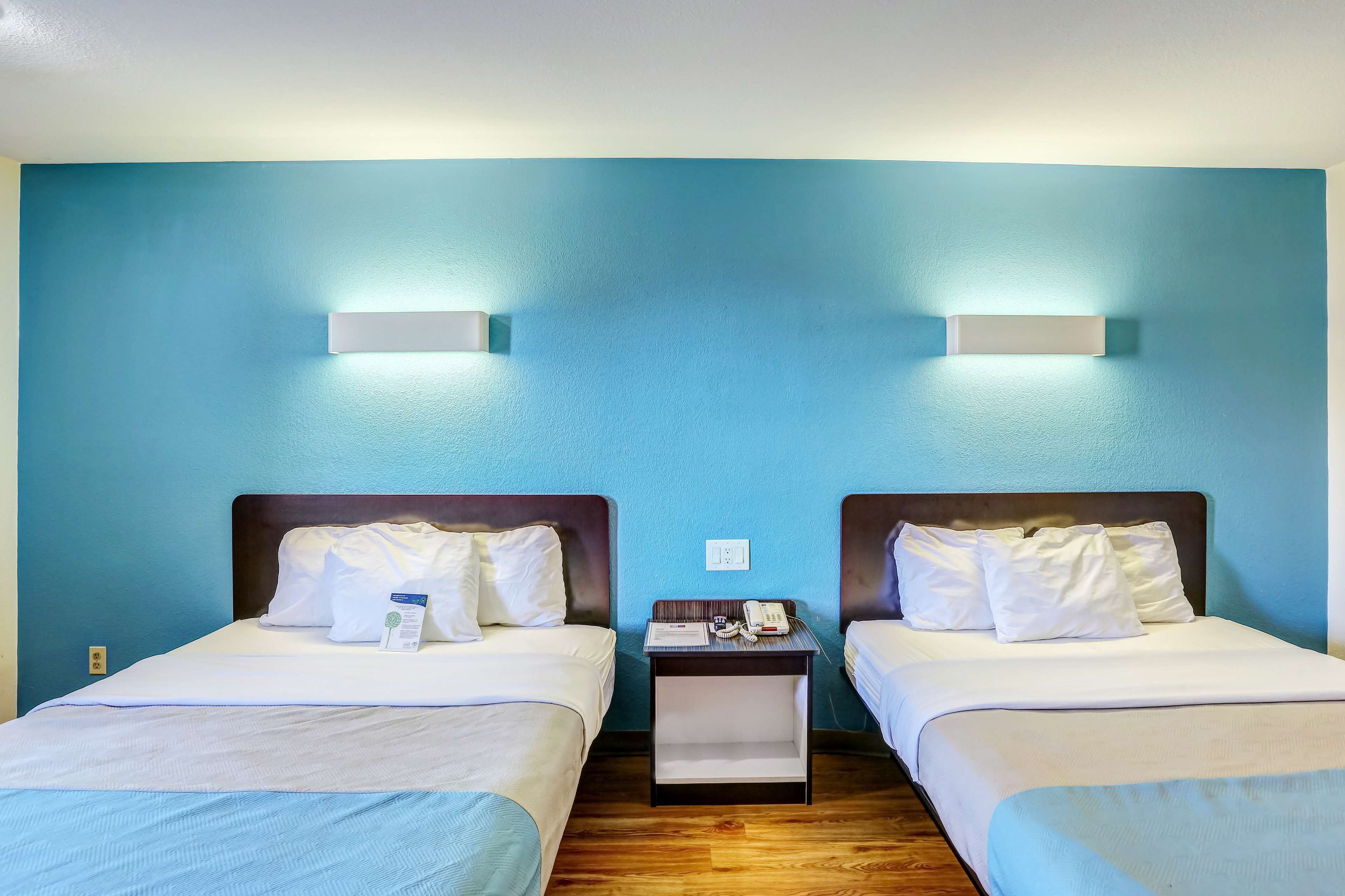 Habitación de hotel con dos camas, una mesita de noche con un teléfono y un libro, y una lámpara de pared.