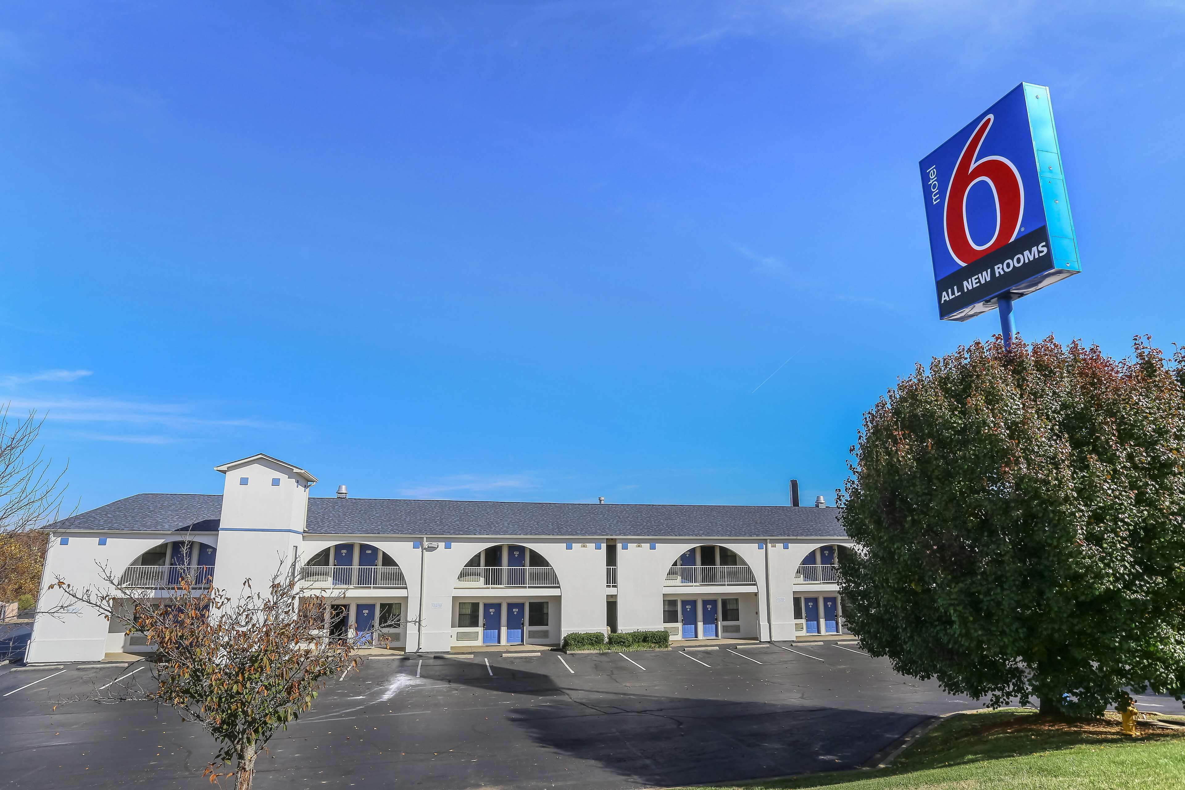A motel with a large sign indicating 6 new rooms. It features a central building with a flat roof and multiple balconies.
