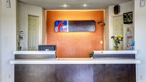 Un mostrador de recepción de hotel con un cartel con el número '6', una pantalla digital y un letrero de 'No fumar'.