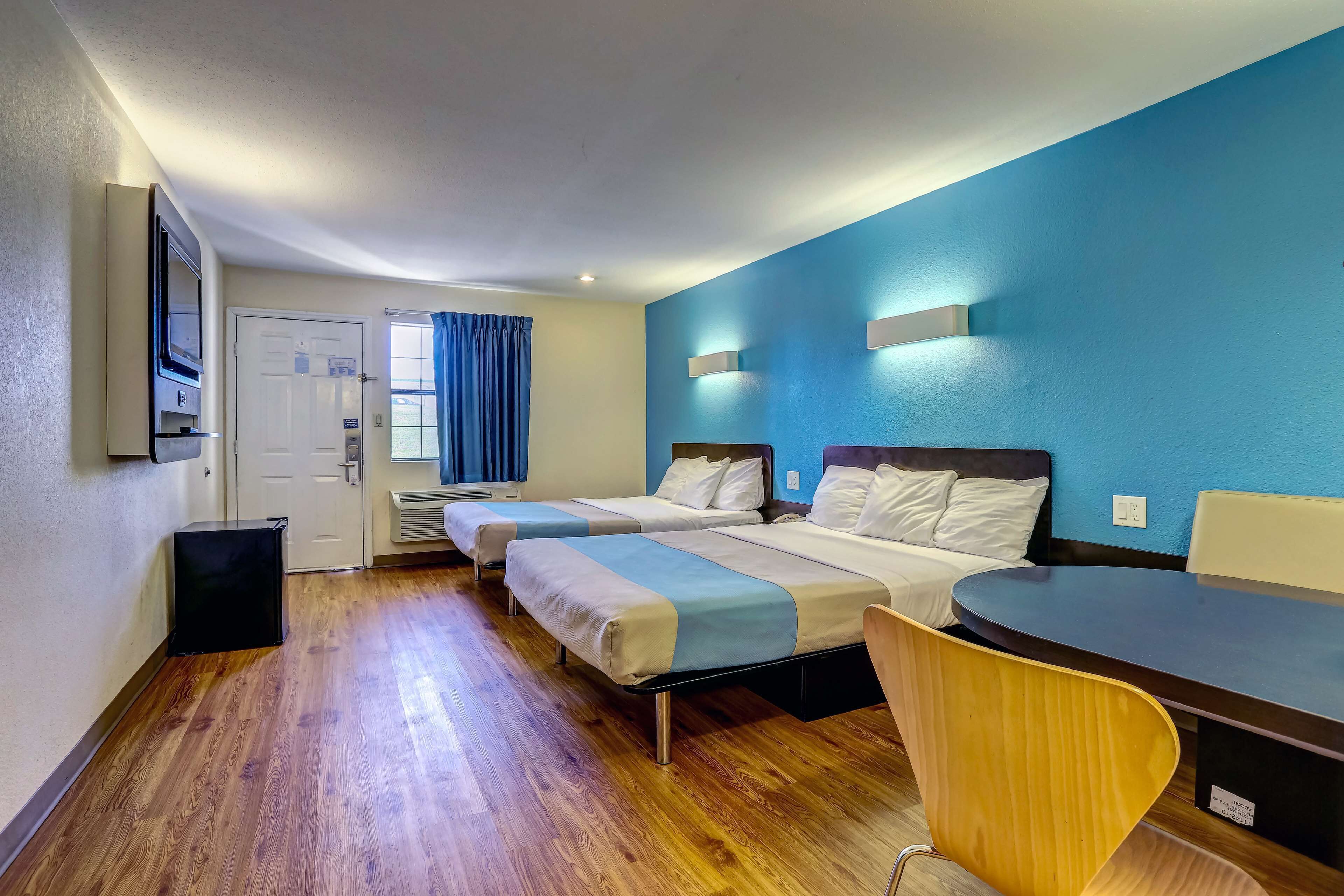 Habitación de hotel con dos camas, un escritorio, una silla, un televisor y una puerta.
