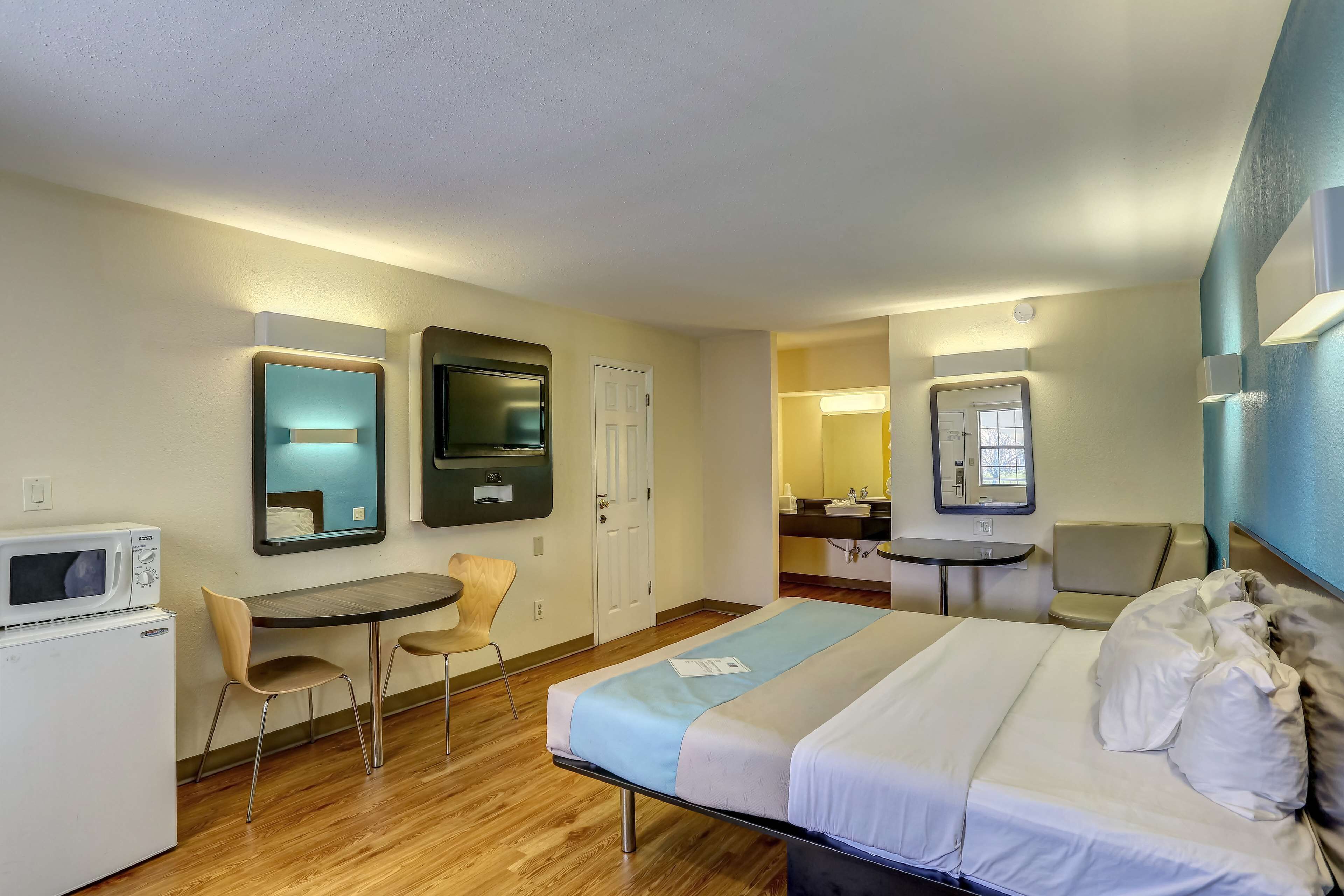 A hotel room with a bed, a desk, a microwave, a chair, and a small table.