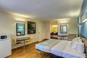 A hotel room with a bed, a desk, a microwave, a chair, and a small table.