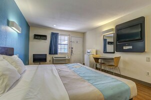 Una habitación de hotel con cama, escritorio, silla, televisor y ventana con cortinas.