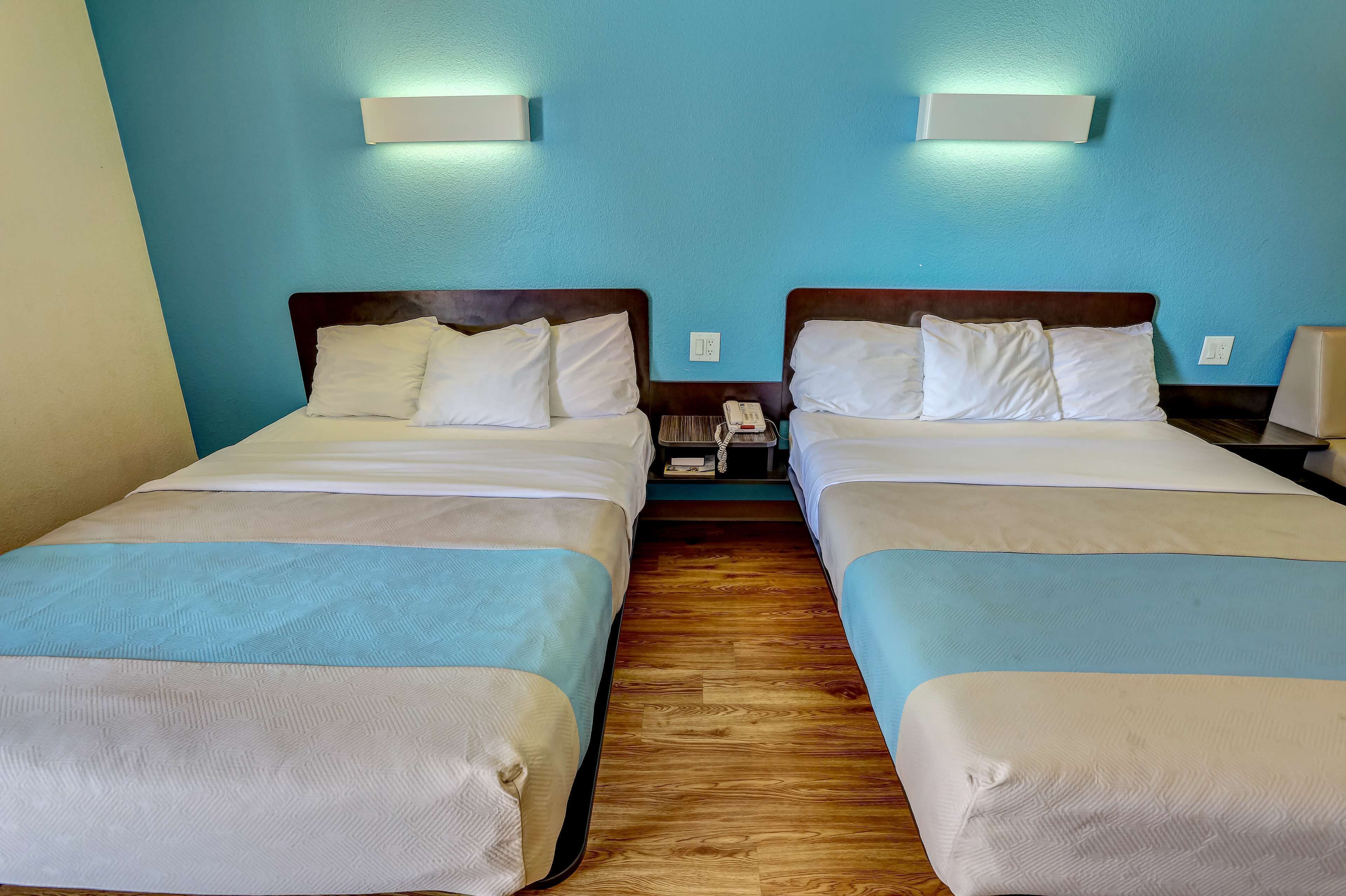 Ein Hotelzimmer mit zwei Betten, jeweils mit weißer Bettwäsche und einem hölzernen Kopfteil. Über jedem Bett befinden sich Wandleuchten.