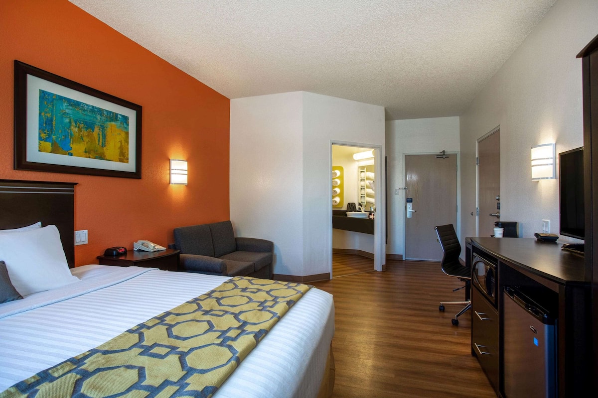 A hotel room with a bed, a desk, a chair, a television, and a bathroom visible through an open door.