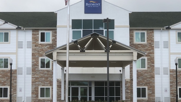 A Baymont Inn & Suites building with a covered entrance, stone facade, and flag. - Baymont Inn & Suites Sheridan (Sheridan)