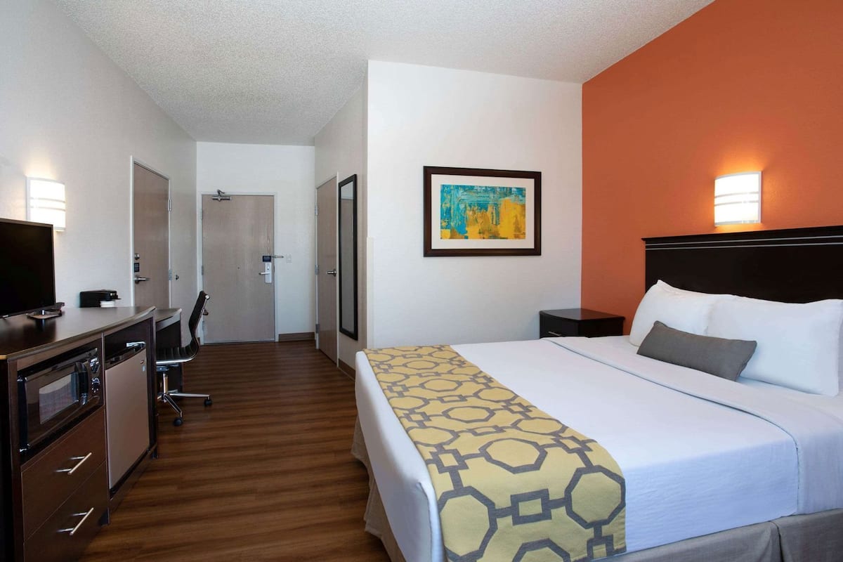 A hotel room with a bed, desk, chair, and a painting on the wall.