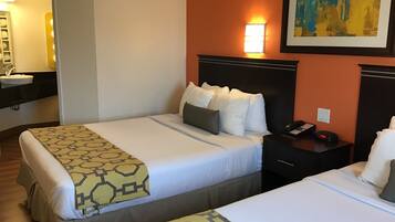 A hotel room with two beds, a bedside table with a phone and alarm clock, a nightstand, a wall-mounted light, and a painting.