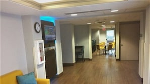 A hotel lobby with a yellow sofa, a clock, a digital screen, and a dining area with yellow chairs. - Baymont Inn & Suites Sheridan (Sheridan)