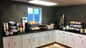 A breakfast bar with various food items and beverages, a window with a view, and a counter with packaged goods. - Baymont Inn & Suites Sheridan (Sheridan)