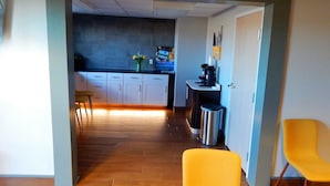 A modern kitchen with white cabinets, a dark backsplash, and a coffee machine. There is a trash can and a small table with a chair. - Baymont Inn & Suites Sheridan (Sheridan)