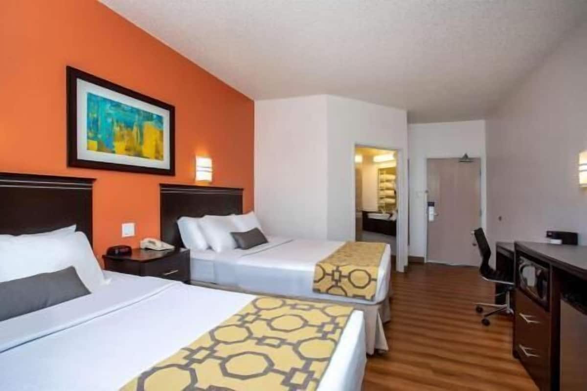 A hotel room with two beds, a desk, a chair, and a painting on the wall.