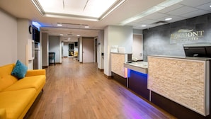 A reception area with a reception desk, a clock, and a yellow sofa. - Baymont Inn & Suites Sheridan (Sheridan)