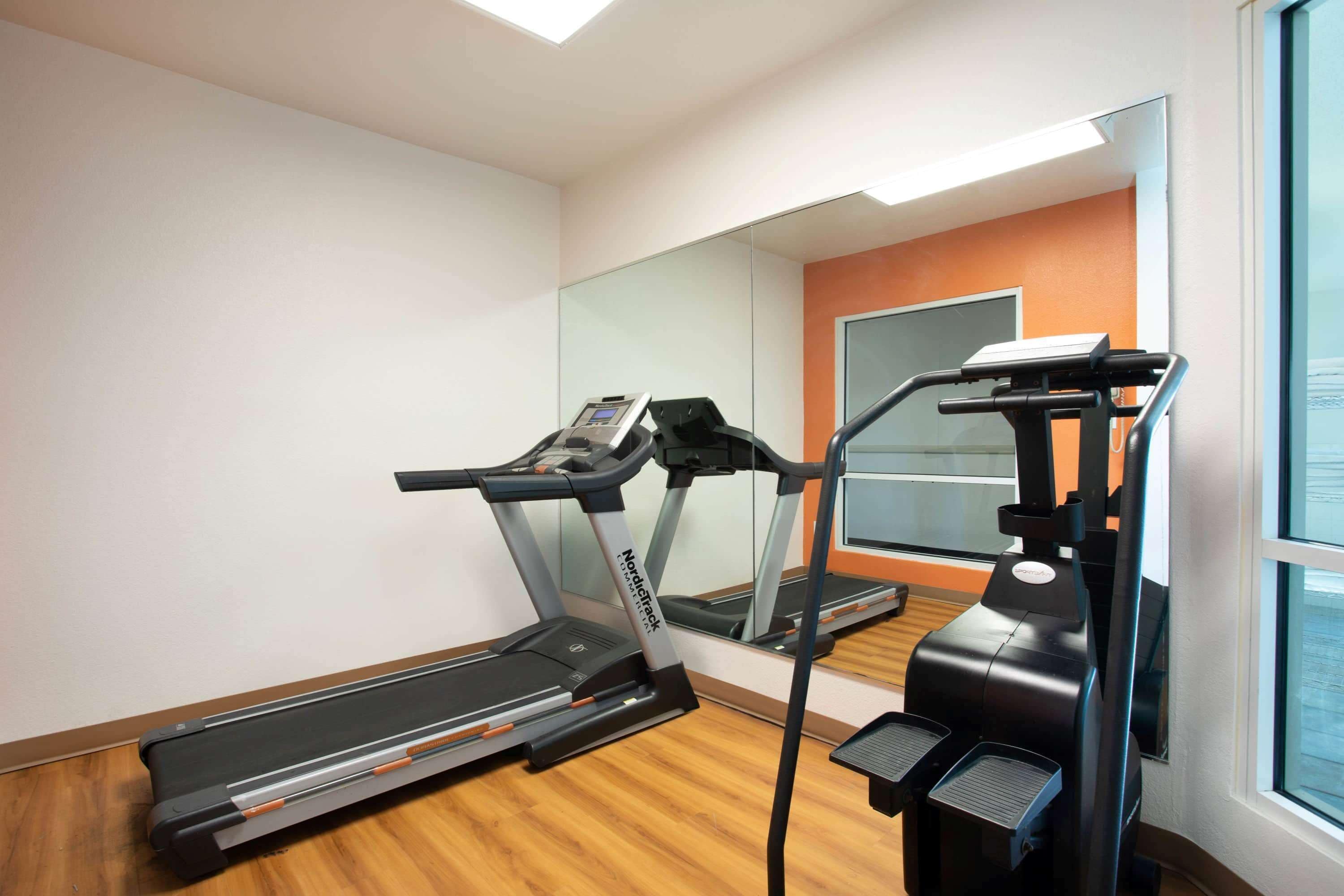 Une salle de sport équipée de tapis de course et d’un vélo d’appartement, d’un grand miroir et d’une fenêtre donnant sur un paysage agréable.