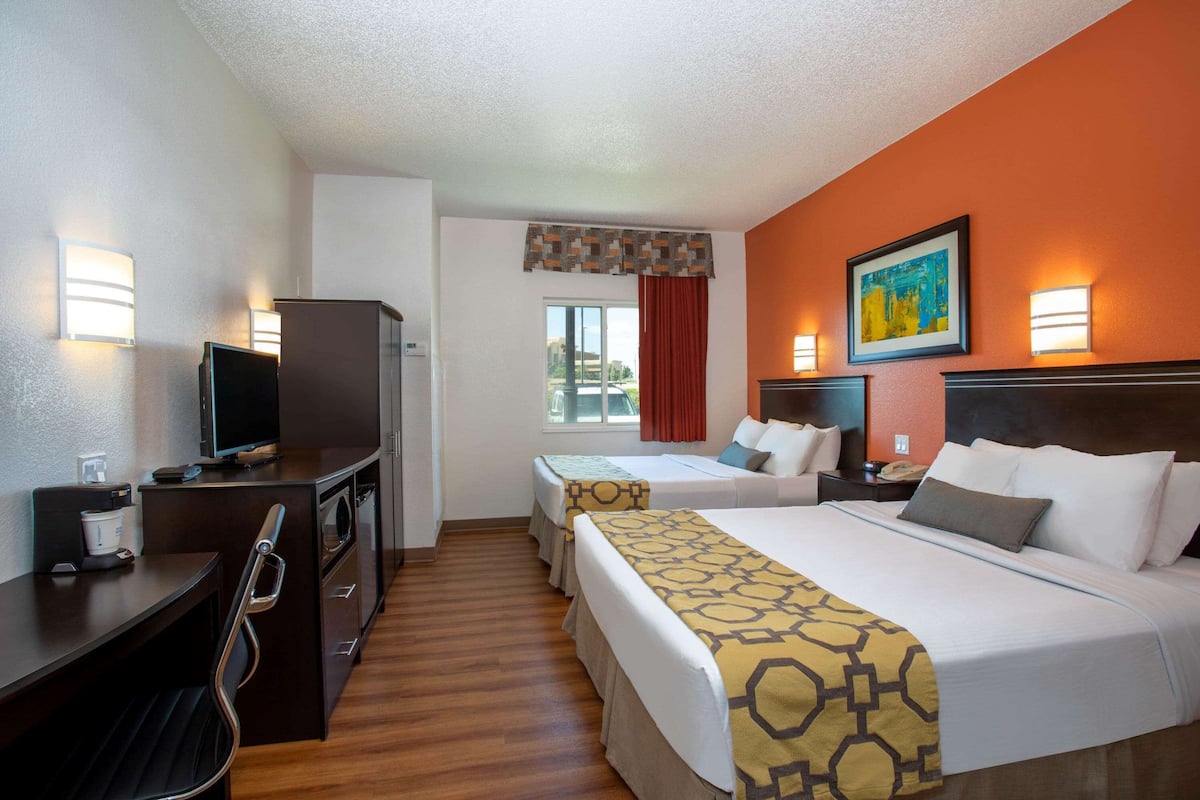 A hotel room with a bed, two bedside tables, a desk with a chair, a television, and a window with curtains.