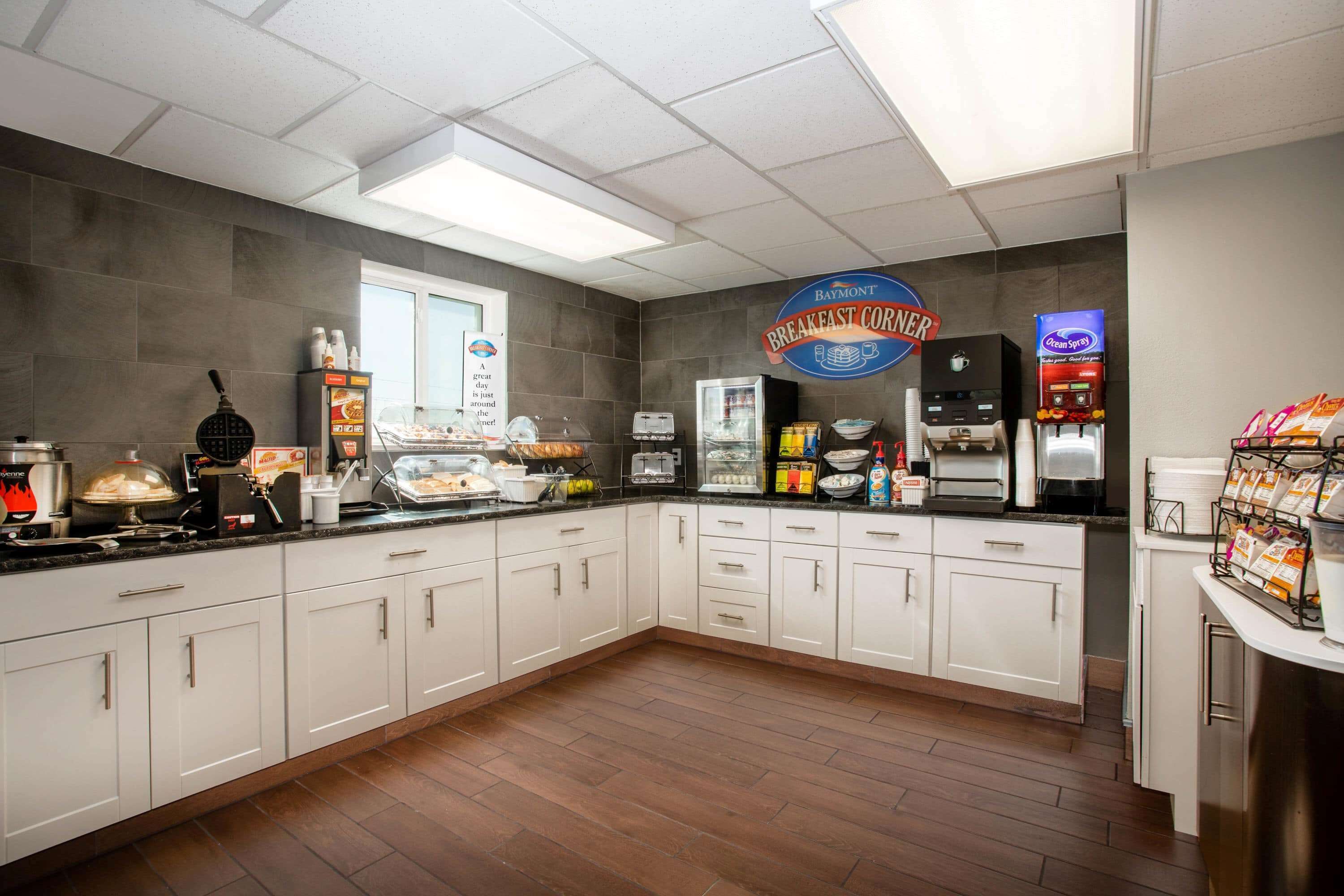 Una barra de desayuno con el letrero de Baymont, una máquina para gofres, una cafetera y un refrigerador con alimentos.