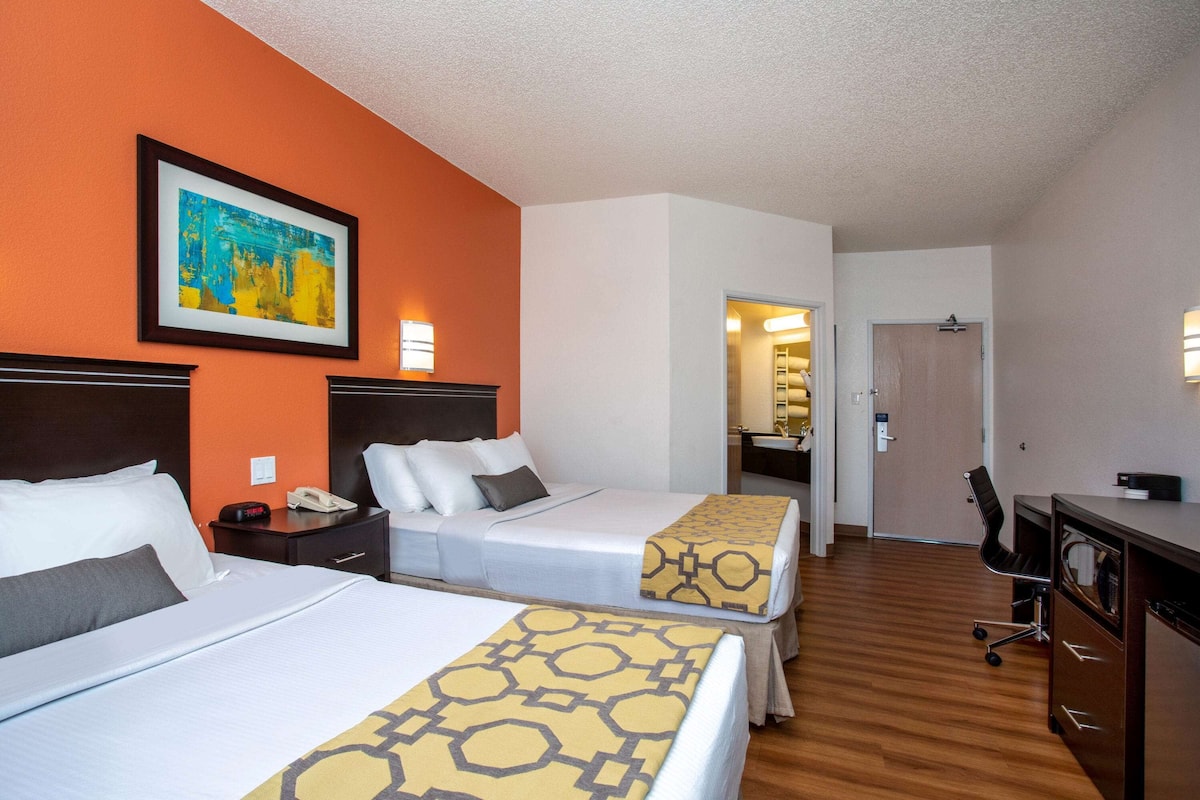 A hotel room with two beds, a desk, a chair, and a bathroom visible through an open door.