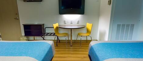 A hotel room with two beds, a small table with two chairs, a TV mounted on the wall, and a wardrobe.