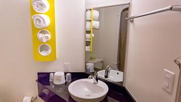 Un baño con un lavamanos blanco, un espejo, un perchero con tres toallas y una encimera morada.