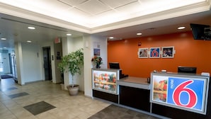 A hotel reception area with a reception desk, a potted plant, and a large sign indicating room number 6. - Motel 6 Pottstown, PA (Pottstown)