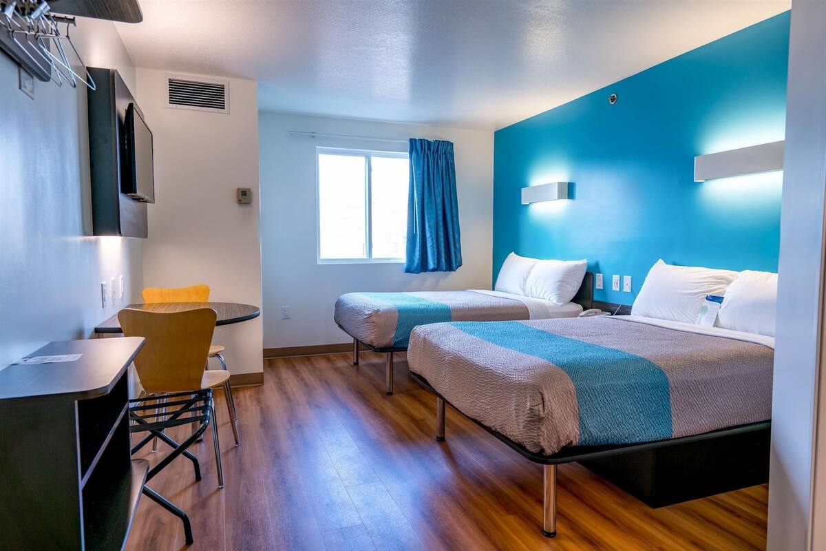 A hotel room with two beds, a desk, and a chair.