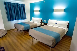 Habitación de hotel con dos camas, suelo de madera, pared azul y una ventana con cortinas azules.