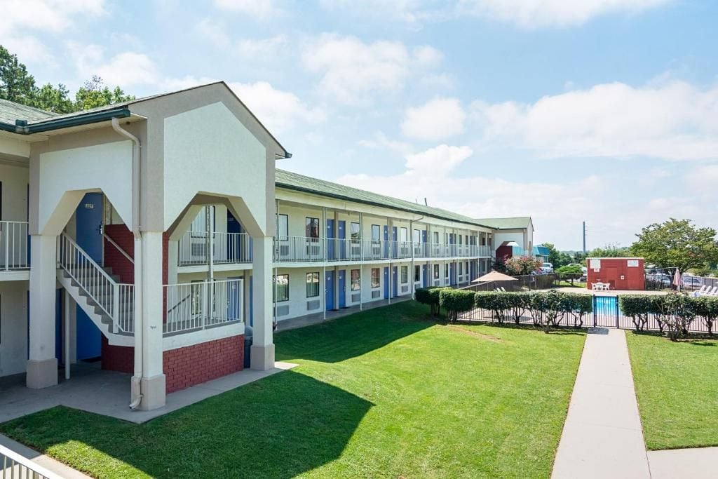 Un motel con pasillo central, habitaciones individuales a cada lado y un pequeño césped.