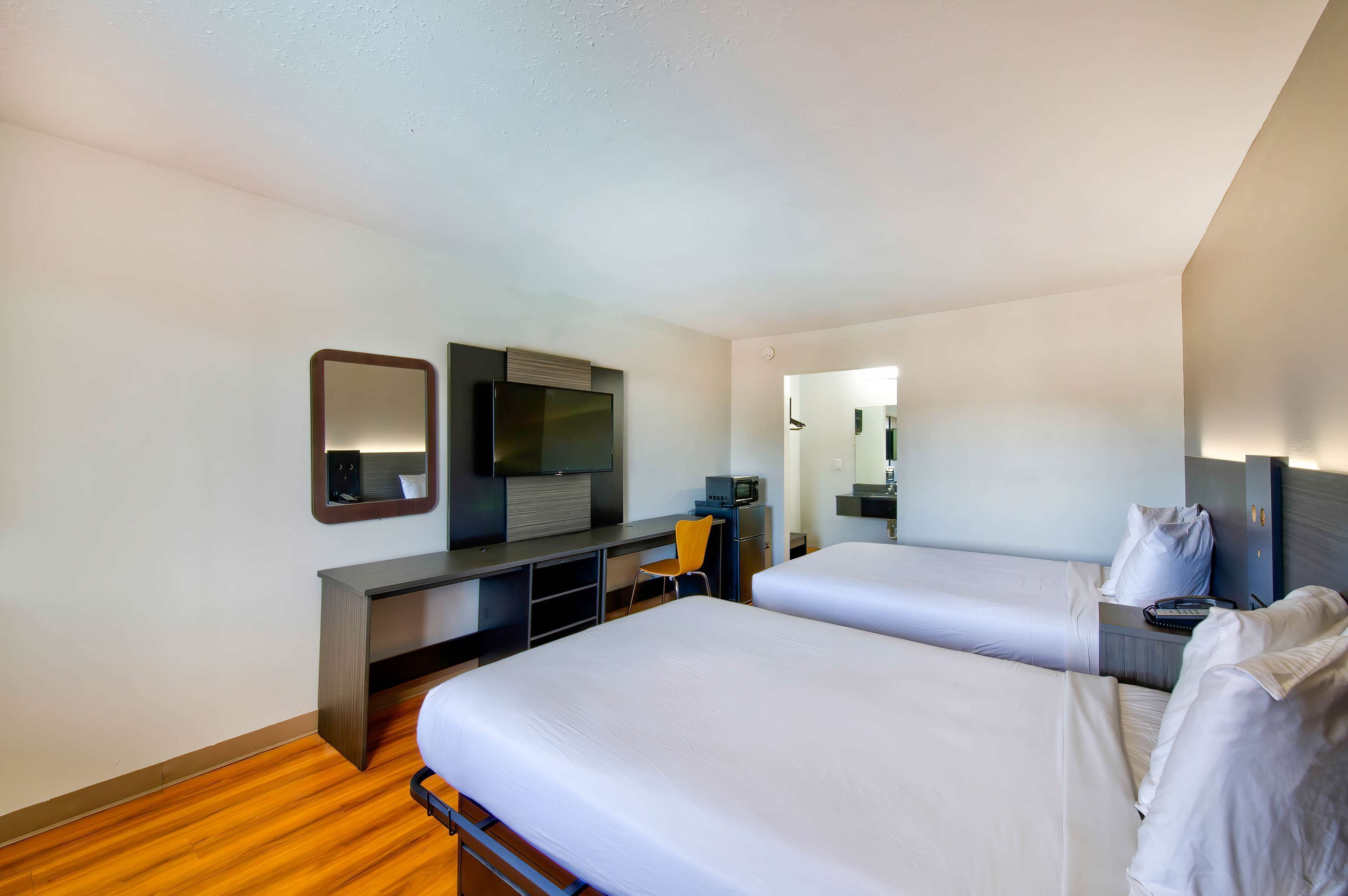 A hotel room with two beds, a desk, a television, and a mirror.