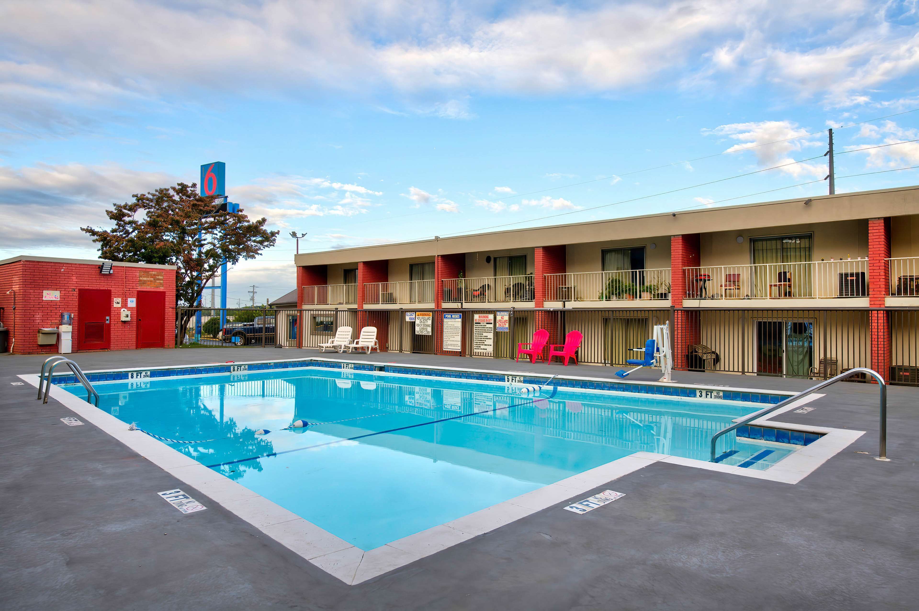 A motel with a swimming pool, multiple balconies, and a red brick building adjacent to it.