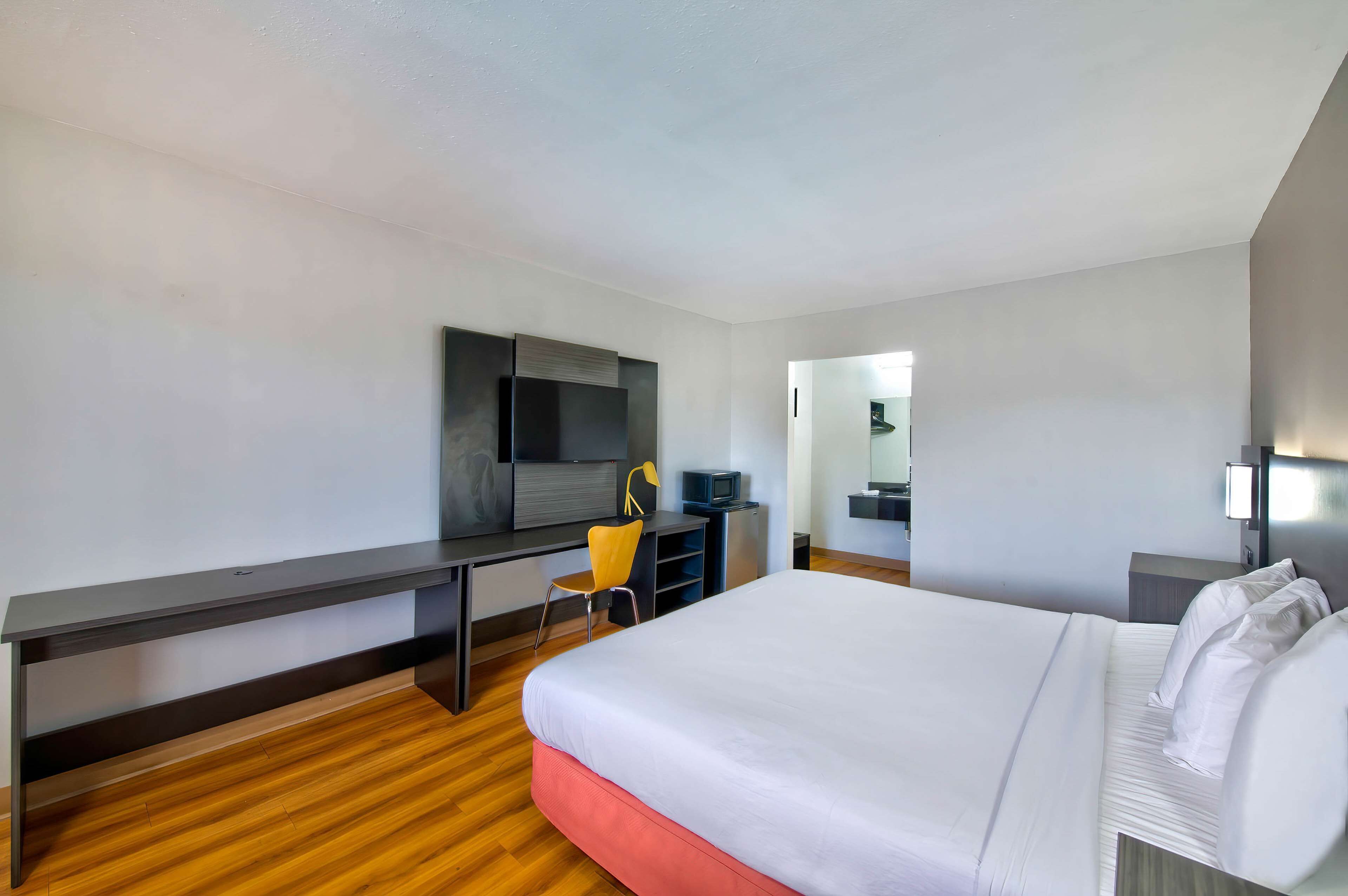 A modern hotel room with a large bed, a desk with a chair, a television, and a wardrobe.