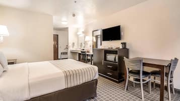 Quarto de hotel com cama, escrivaninha, duas cadeiras, televisão e micro-ondas.