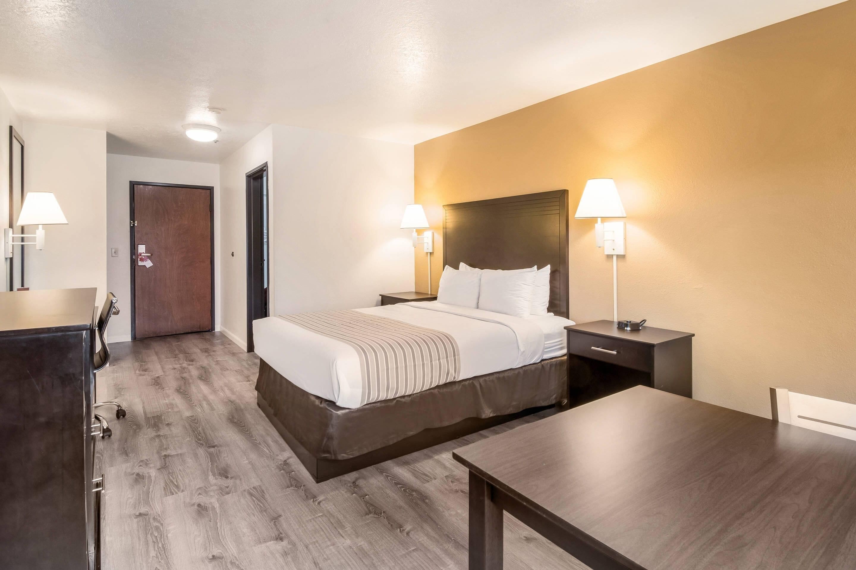Una habitación de hotel con una cama, mesitas de noche, un escritorio y un armario.