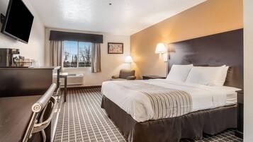 A hotel room with a bed, desk, chair, TV, and a window with curtains.