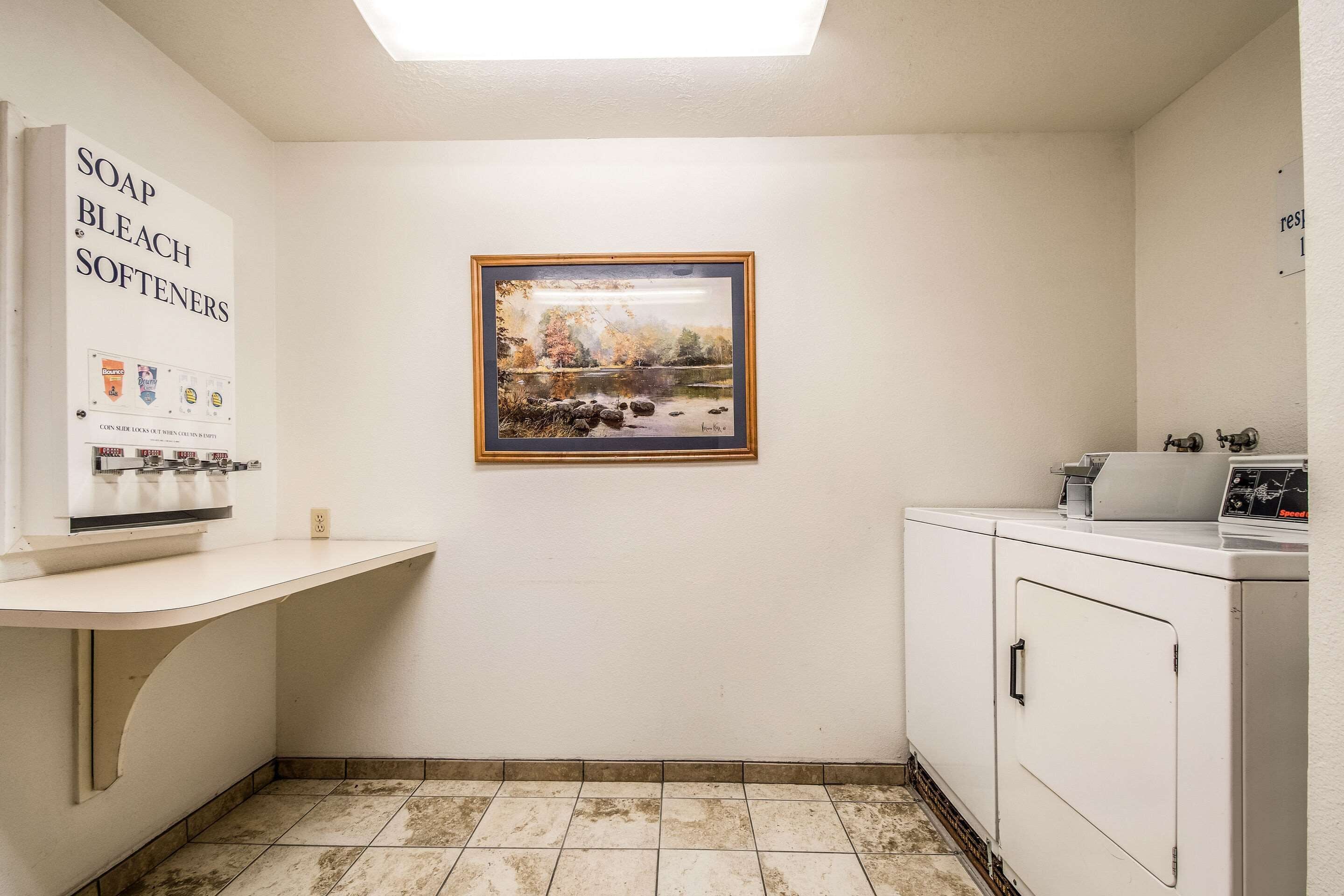 A laundry room with a sink, a washing machine, and a framed painting on the wall.
