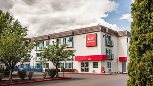 Un edificio de EconoLodge de dos pisos, con una decoración en rojo y blanco, un área de estacionamiento con portón y un cielo despejado.