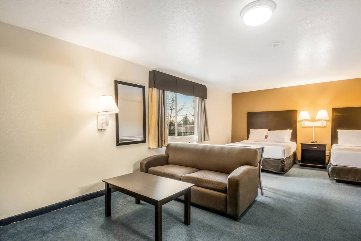 Una habitación de hotel con sofá, una mesita, dos camas y una mesita de noche con lámparas.