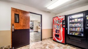 Un vestíbulo de hotel con una puerta de madera, una máquina expendedora con la marca Coca-Cola y otra máquina expendedora de aperitivos.