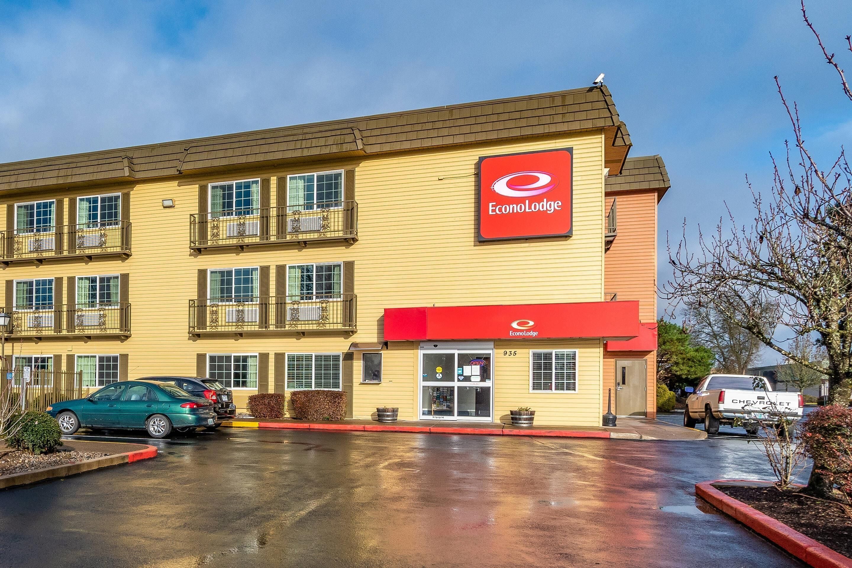 A two-story EconoLodge building with a red awning, a parking lot with cars, and a Chevrolet truck parked outside.