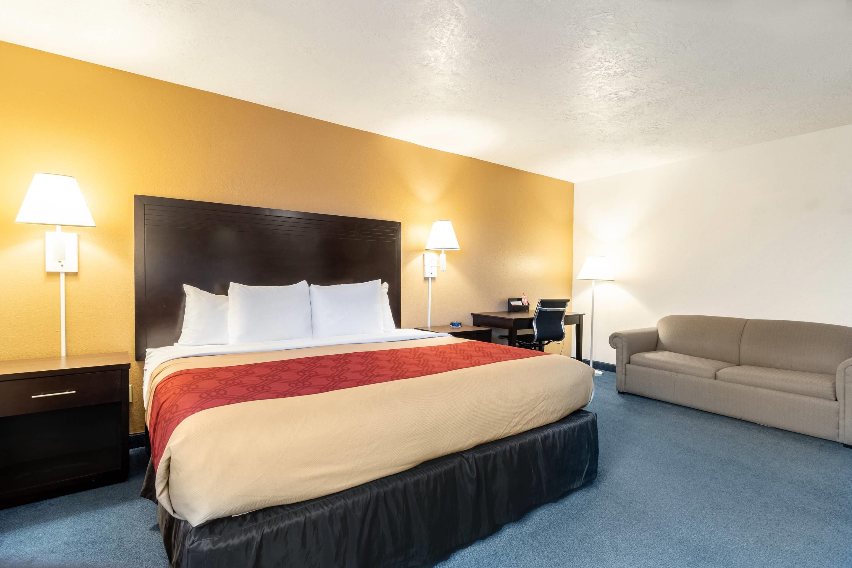 A hotel room with a large bed, two bedside tables, a desk, a chair, and a sofa.
