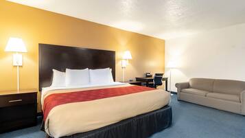 A hotel room with a large bed, two bedside tables, a desk, a chair, and a sofa.