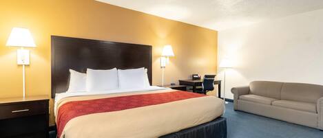 A hotel room with a large bed, two bedside tables, a desk, a chair, and a sofa.