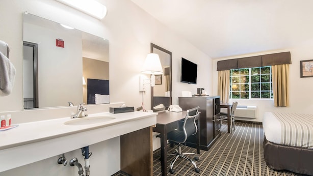 Habitación de hotel con un tocador grande, un escritorio con silla, una cama y un ventanal con cortinas.