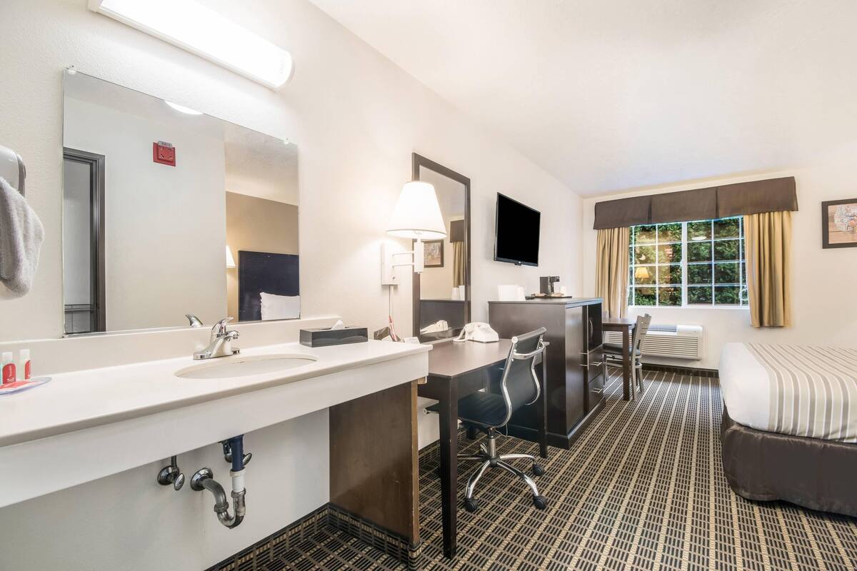 Habitación de hotel con un tocador grande, un escritorio con silla, una cama y un ventanal con cortinas.