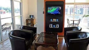 A seating area with a television screen, a table, and chairs. - Motel 6 Sallisaw, OK (Sallisaw)